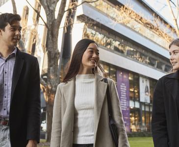 Three students wearing winter clothing walking on lower campus