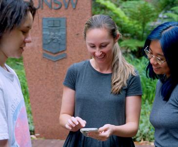 Three students looking down at a smartphone