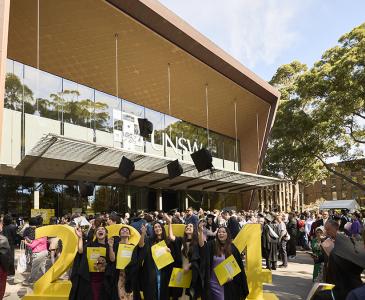Graduates in gowns outside the Clancy Auditorium, throwing their mortarboards in the air