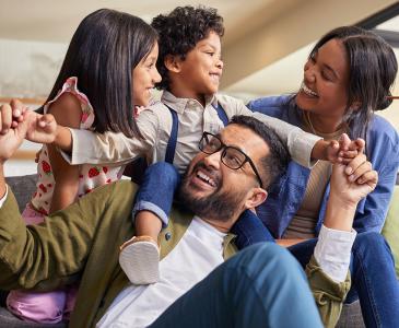 A family smiling together, with the kids and mum on a sofa and dad on the floor in front of them