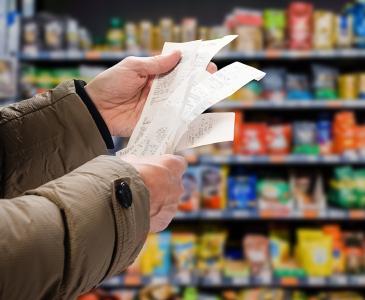 Close up of a person holding multiple shopping receipts with a supermarket shelf in the background
