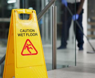 A yellow sign showing the words "Caution wet floor" with a blurry person mopping in the background