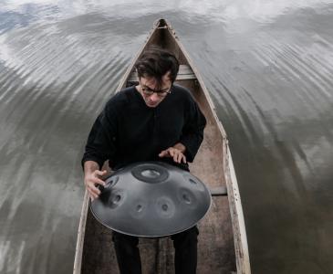 Baran Yildiz playing the handpan surrounded by water.