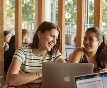 Two students smiling while using a laptop