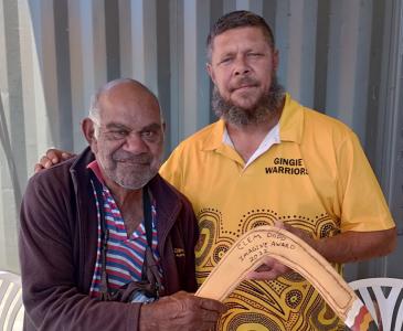 Clem Dodd (Dharriwaa Elders Group [DEG] Speaker) is presented with a bubarraa (fighting boomerang) by Steven “Bungee” Dennis, a Dealing with Fines team member at the DEG.