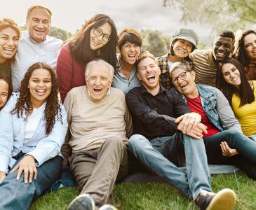 A group of smiling people sitting on grass with an elderly man at the centre