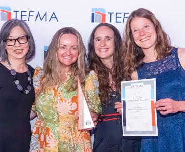 Four women smiling while one holds a certificate