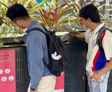 Two students putting rubbish in a bin