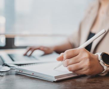 Close up of woman writing in notebook beside laptop