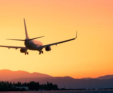 An airplane in silhouette against an orange sky