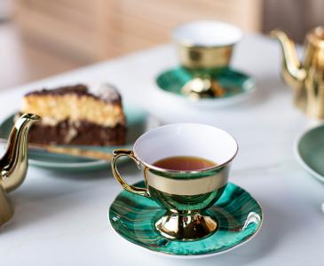 Green tea cup with black tea, a plate with cake, and a golden tea pot on a table