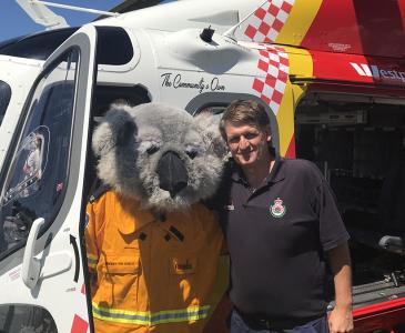 Mark Griffith standing beside a person in a koala suit in front of a rescue helicopter