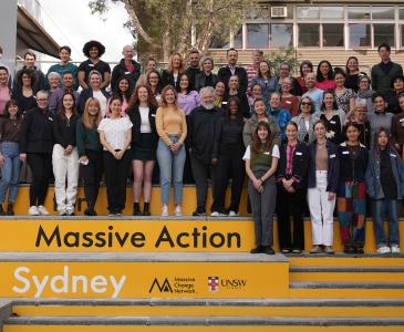 Large group of people standing on yellow steps reading Massive Action Sydney