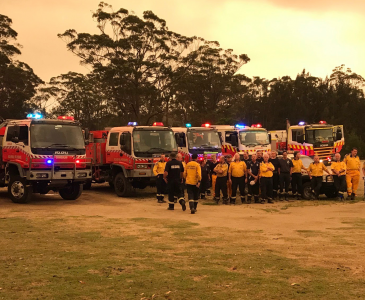 Fire trucks lined up in an open green lawn with firefighters standing in front