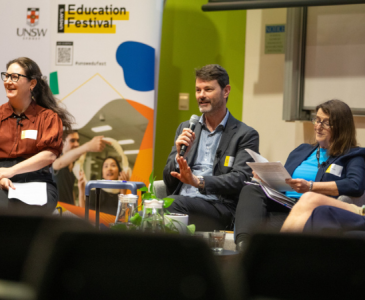 A man holds a microphone sitting beside two women wearing glasses for a panel discussion