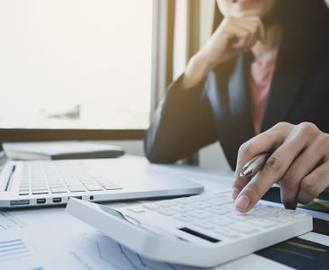 Laptop and calculator on a desk with woman's hand on calculator