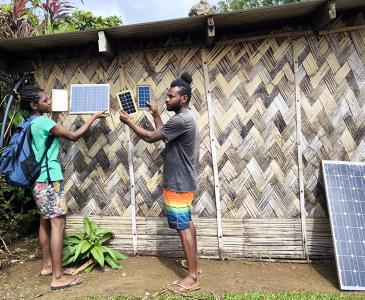 Two people standing and holding small solar panels outside a building