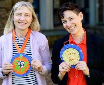 Two women smiling and wearing paper rosettes