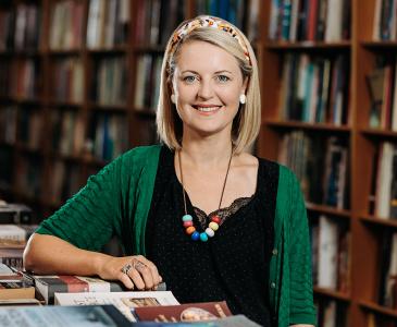 Sarah Sassoon in front of a bookshelf at a table covered in books