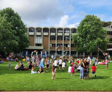 Crowds of adults and children gather for games on a lawn in front of a three-story building