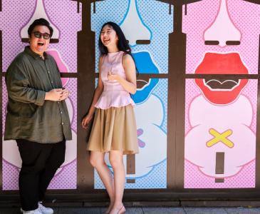 Two people standing and laughing in front of a pop art painted wall.