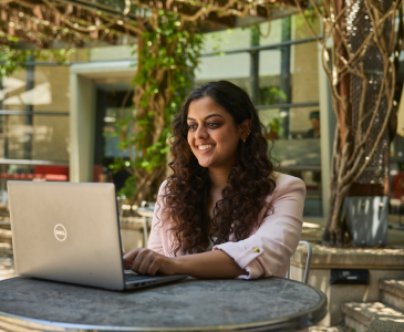 A woman sitting at an outside table and working on a computer.
