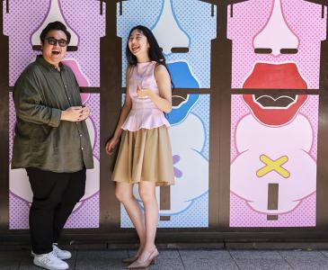 Two people standing against a colourful wall