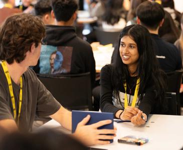 A group of people wearing yellow lanyards sit at tables