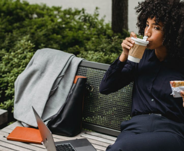 Woman eating and drinking with laptop on bench