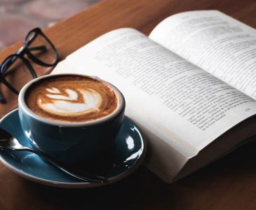 A cup of coffee, open book and glasses on a table