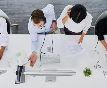 View from above of four people sitting at a white desk working on computers