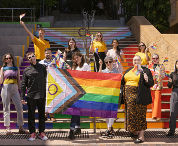 A group of people gathered on the Basser steps with a Progress Pride flag