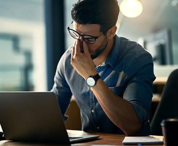 A man sits at a desk with his hand at his face looking stressed