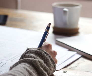 Person writing with a cup of coffee on their desk