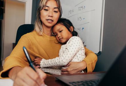 A young woman writing with a child sitting on her lap