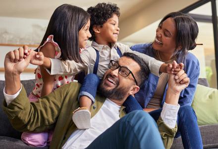 A family smiling together, with the kids and mum on a sofa and dad on the floor in front of them