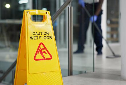 A yellow sign showing the words "Caution wet floor" with a blurry person mopping in the background