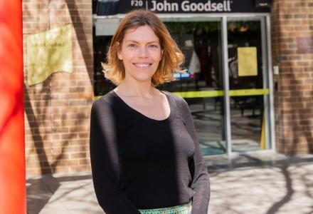 A woman wearing a black jumper stands out the front of a building