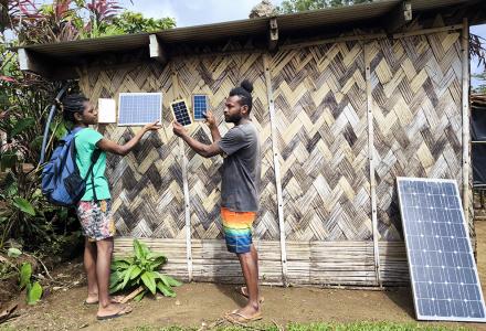 Two people standing and holding small solar panels outside a building