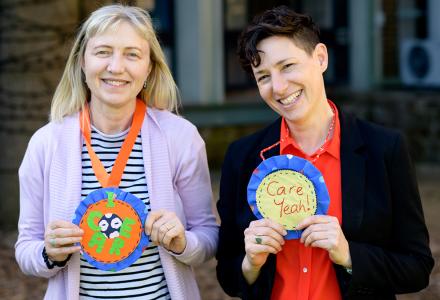 Two women smiling and wearing paper rosettes