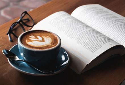 A cup of coffee, open book and glasses on a table