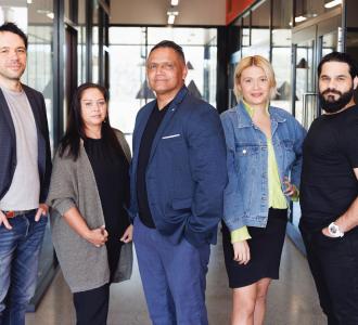 Five Aboriginal Australians stand in front of a modern office building