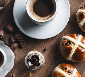 Hot cross buns on a wooden bench beside white cup with coffee