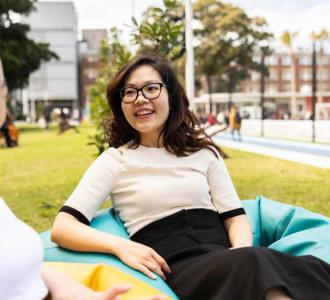 A woman wearing glasses sits on a beanbag talking to another woman outdoors.