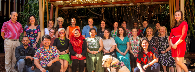 A large group of course attendees posed beneath a wooden shelter at Charles Darwin University 