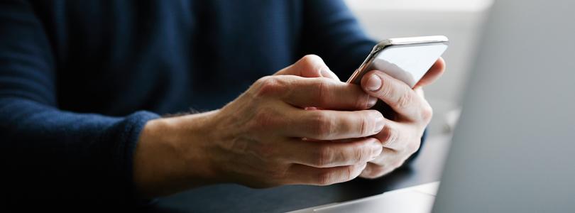 Close up of a person's hands holding a mobile phone while sitting at a laptop