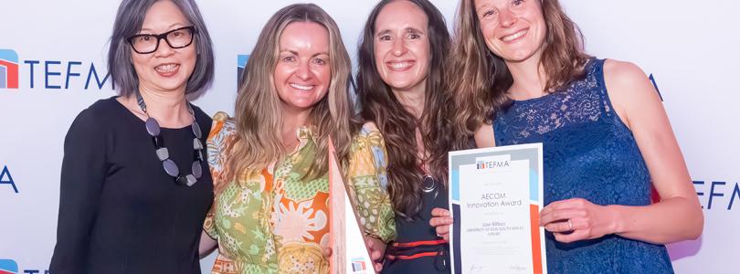 Four women smiling while one holds a certificate