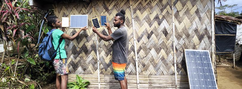 Two people standing and holding small solar panels outside a building