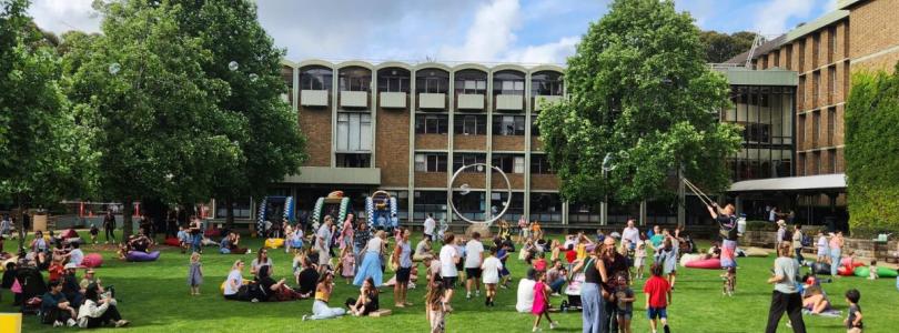 Crowds of adults and children gather for games on a lawn in front of a three-story building